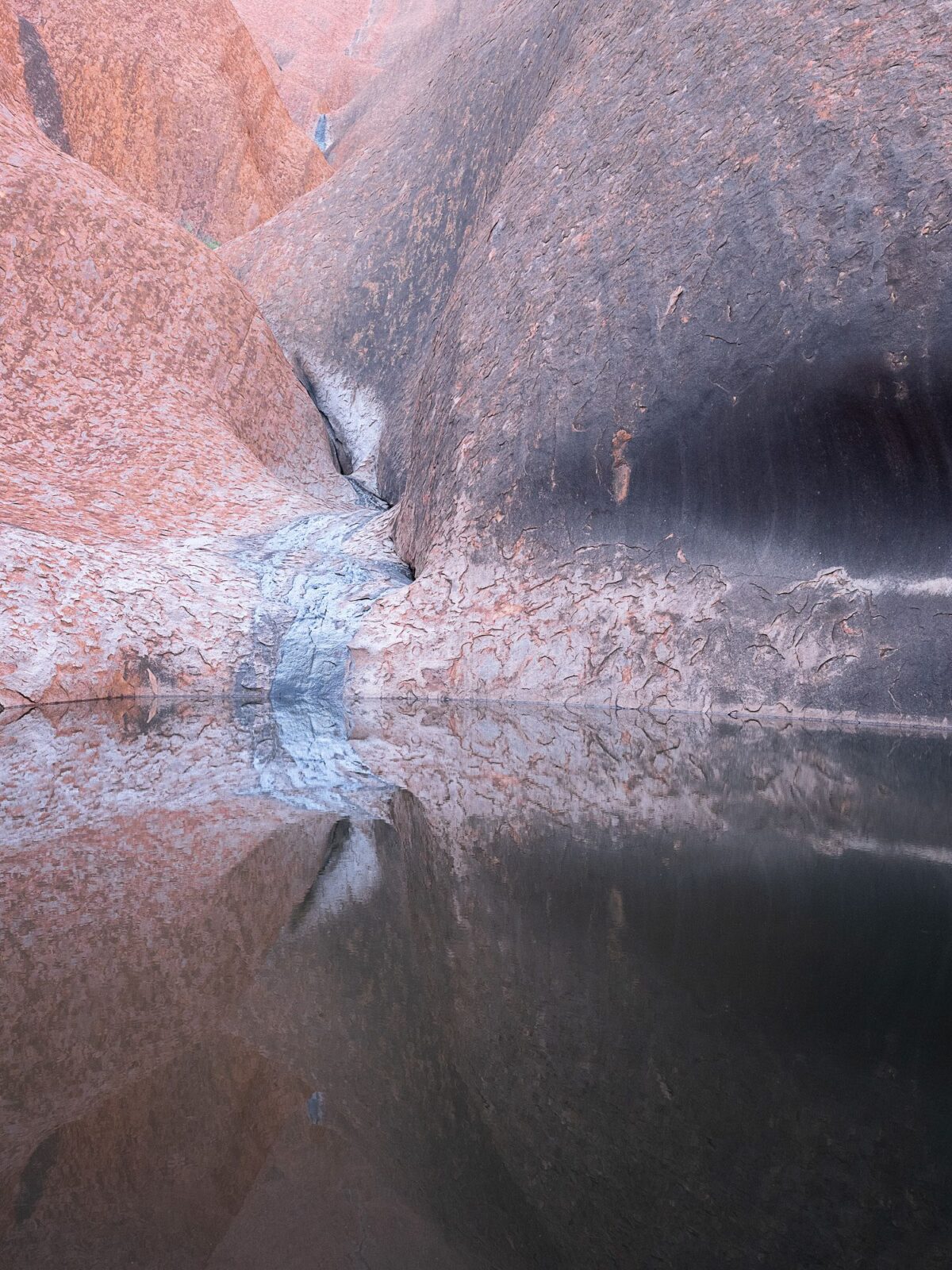 Felslandschaft mit großen, glatten Felsformationen, die sich in einem ruhigen Gewässer spiegeln. (KI-generierte Beschreibung)