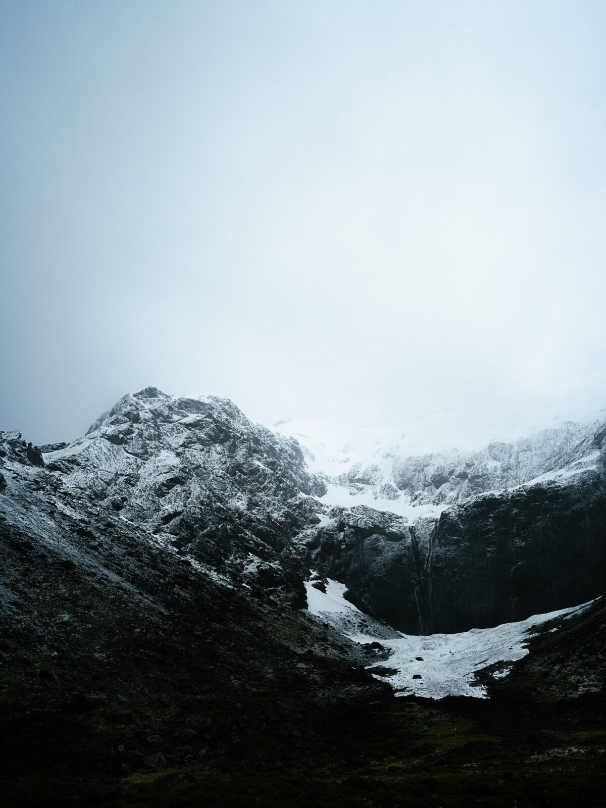 Schneebedeckte Berggipfel unter einem bewölkten Himmel, mit weißen Schneeflecken auf dunklem Gestein. (KI-generierte Beschreibung)