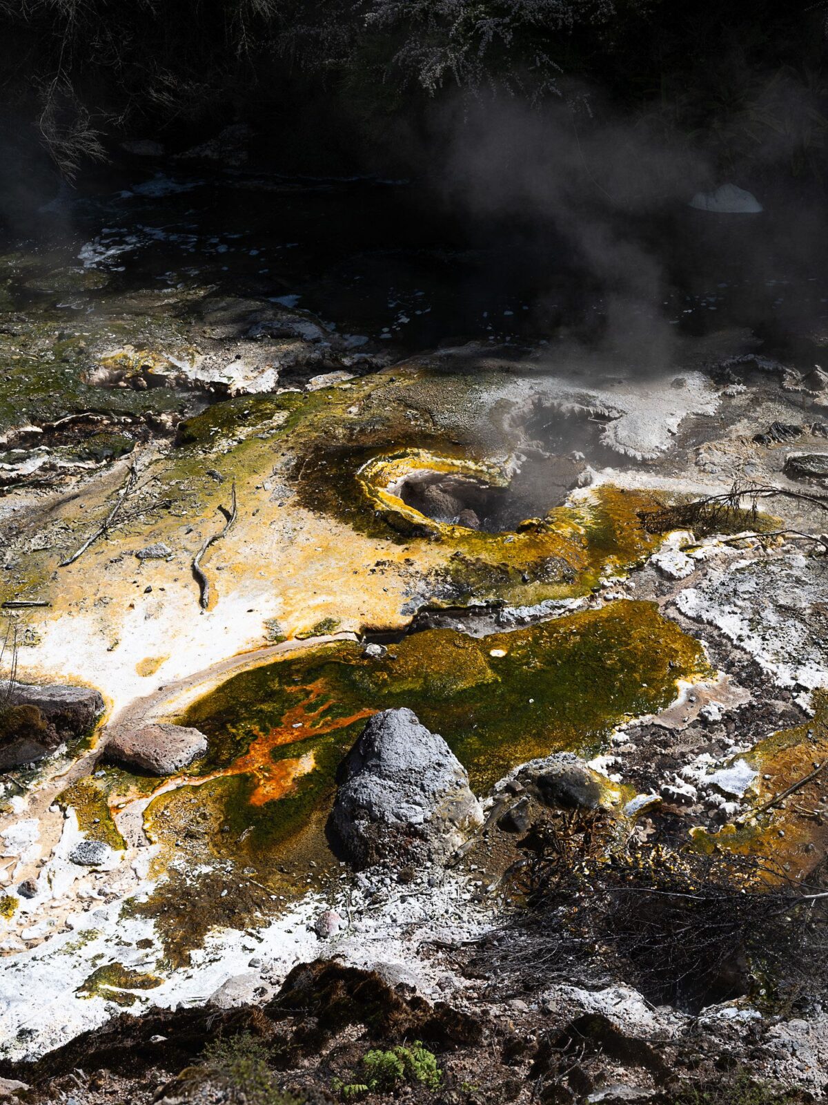 Ein geothermisches Gebiet, in dem Dampf aus farbenfrohen Mineralvorkommen aufsteigt und auf felsigem Gelände orange und gelbe Farbtöne aufweist. (KI-generierte Beschreibung)