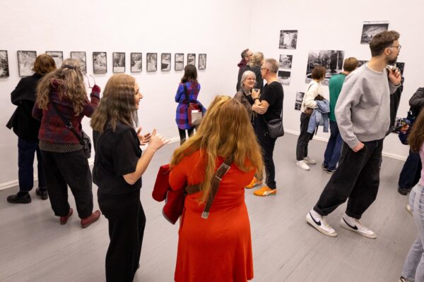 Während einer Kunstausstellung betrachten und diskutieren Menschen Schwarz-Weiß-Fotografien, die auf weißen Galeriewänden ausgestellt sind. (KI-generierte Beschreibung)