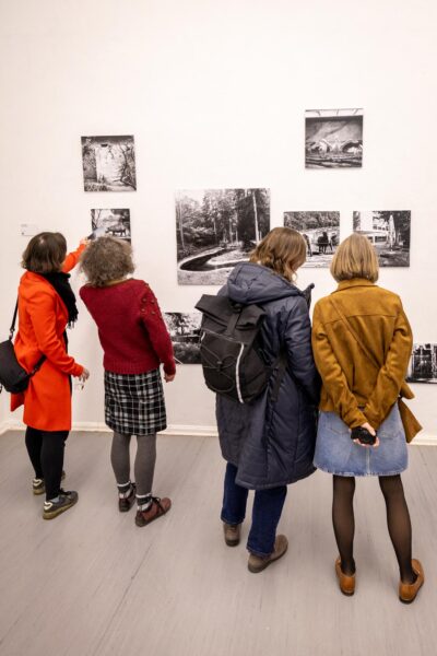 Vier Personen stehen vor einer weißen Wand und betrachten Schwarz-Weiß-Fotografien, die in einer Galerie ausgestellt sind. (KI-generierte Beschreibung)