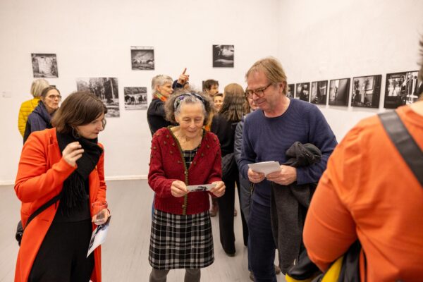 Eine Gruppe von Menschen betrachtet und diskutiert Schwarz-Weiß-Fotografien, die während einer Ausstellung an einer Galeriewand hängen. (KI-generierte Beschreibung)